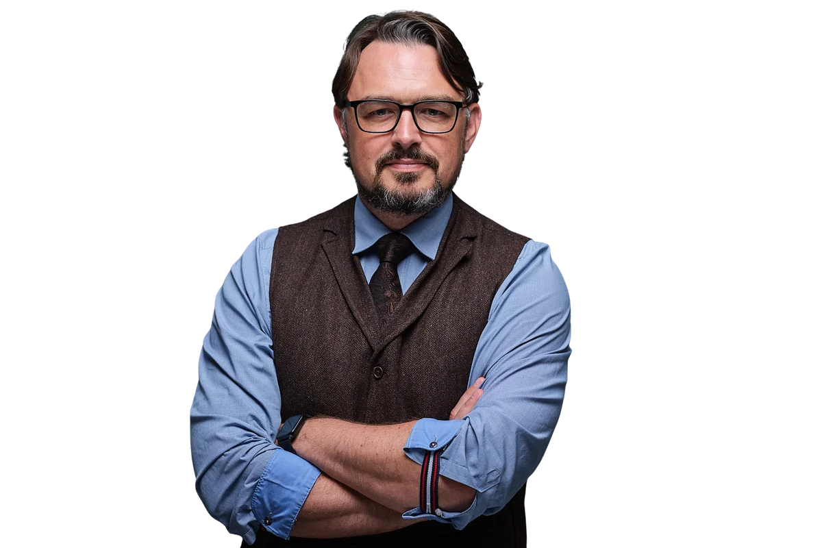 Porträt von Holger Heinze: mit verschränkten Armen, Brille, blauem Hemd und brauner Weste.